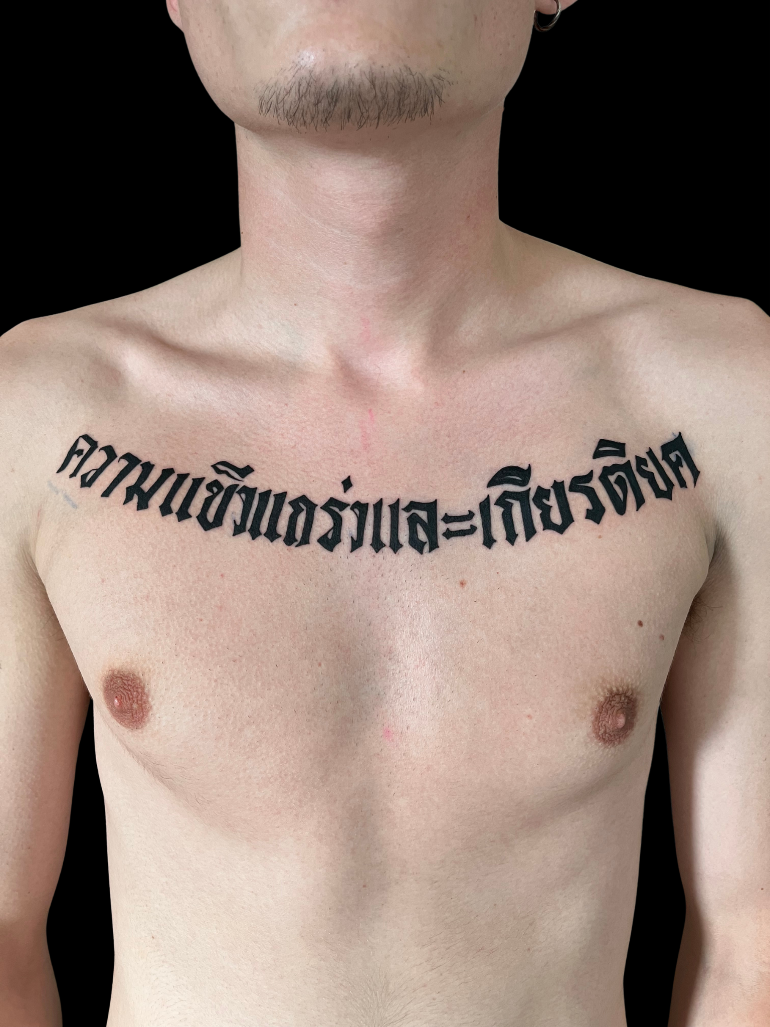 Tatouage lettrage script thaï en blackwork sur le torse — Akamoa Tattoo Moustiers-Sainte-Marie